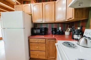 Cocina compacta con armarios de madera, un refrigerador blanco, un microondas, una cafetera y una estufa.