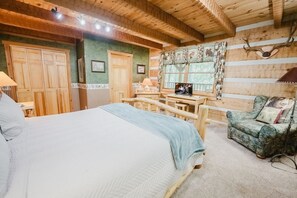 Interior de una cabaña de madera con una cama, un escritorio, una silla y un televisor.