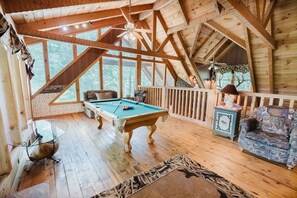 Un interior de madera con una mesa de billar, un sofá y un ventilador de techo.