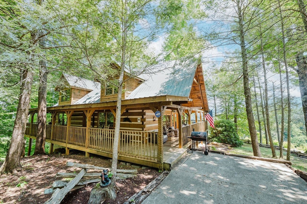 Een chalet met een veranda, een terras en een barbecueplaats, omgeven door bomen.