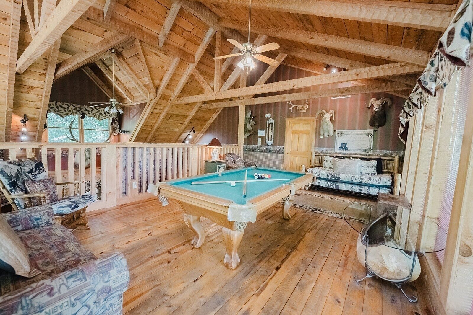 A cozy wooden room with a pool table, a sofa, and a ceiling fan.