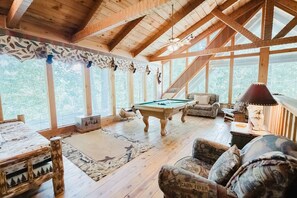Un interior de madera con mesa de billar, sofás y un ventanal grande.