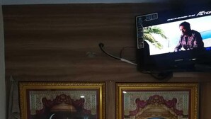 Dues teles emmarcades amb temàtica religiosa a la paret, un televisor a dalt i una espelleta petita a l'estant de sota.