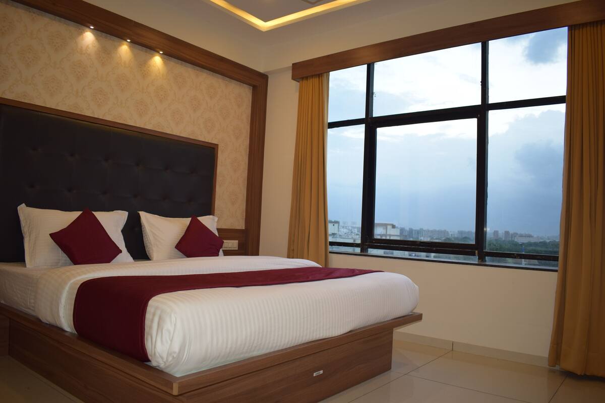 Una habitación de hotel moderna con una cama grande, cabecera, ventana con cortinas y vista a la ciudad.