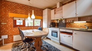 Une cuisine avec un mur en briques, des meubles blancs, une table à manger avec des chaises et un poêle.