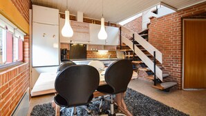 Une cuisine compacte avec des meubles blancs, un coin repas avec des chaises noires et un escalier menant à un niveau supérieur.