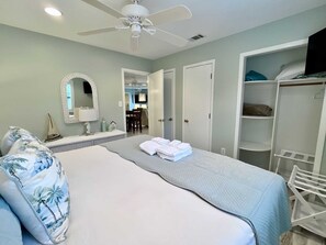 Une chambre à coucher avec un lit, un ventilateur de plafond, une armoire et une salle de bain visible à travers une porte ouverte.