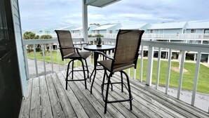 Een houten terras met twee stoelen en een tafel, met uitzicht op een rij blauwe huizen met witte hekwerken.