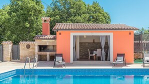 Un espace aménagé au bord de la piscine, avec un barbecue en pierre, des sièges d’extérieur et une vue sur la piscine.