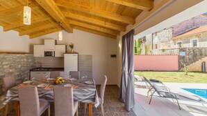 Un coin repas avec une table dressée pour quatre personnes, une cuisine équipée d’appareils électroménagers modernes et une vue sur une piscine et un jardin.