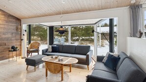 Ein modernes Wohnzimmer mit einer grauen Couch, einem runden Holztisch und einem Korbstuhl.