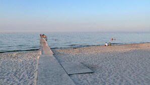 Ein Sandstrand mit einer hölzernen Mole, die sich über ruhiges Wasser erstreckt.