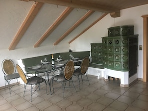 Un coin repas avec une table dressée pour six personnes, entourée de chaises en osier, sous un plafond en pente avec des poutres en bois.