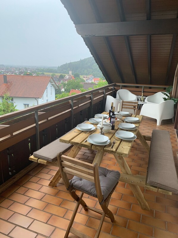 A terrace with a wooden table set for dining, surrounded by chairs and benches.
