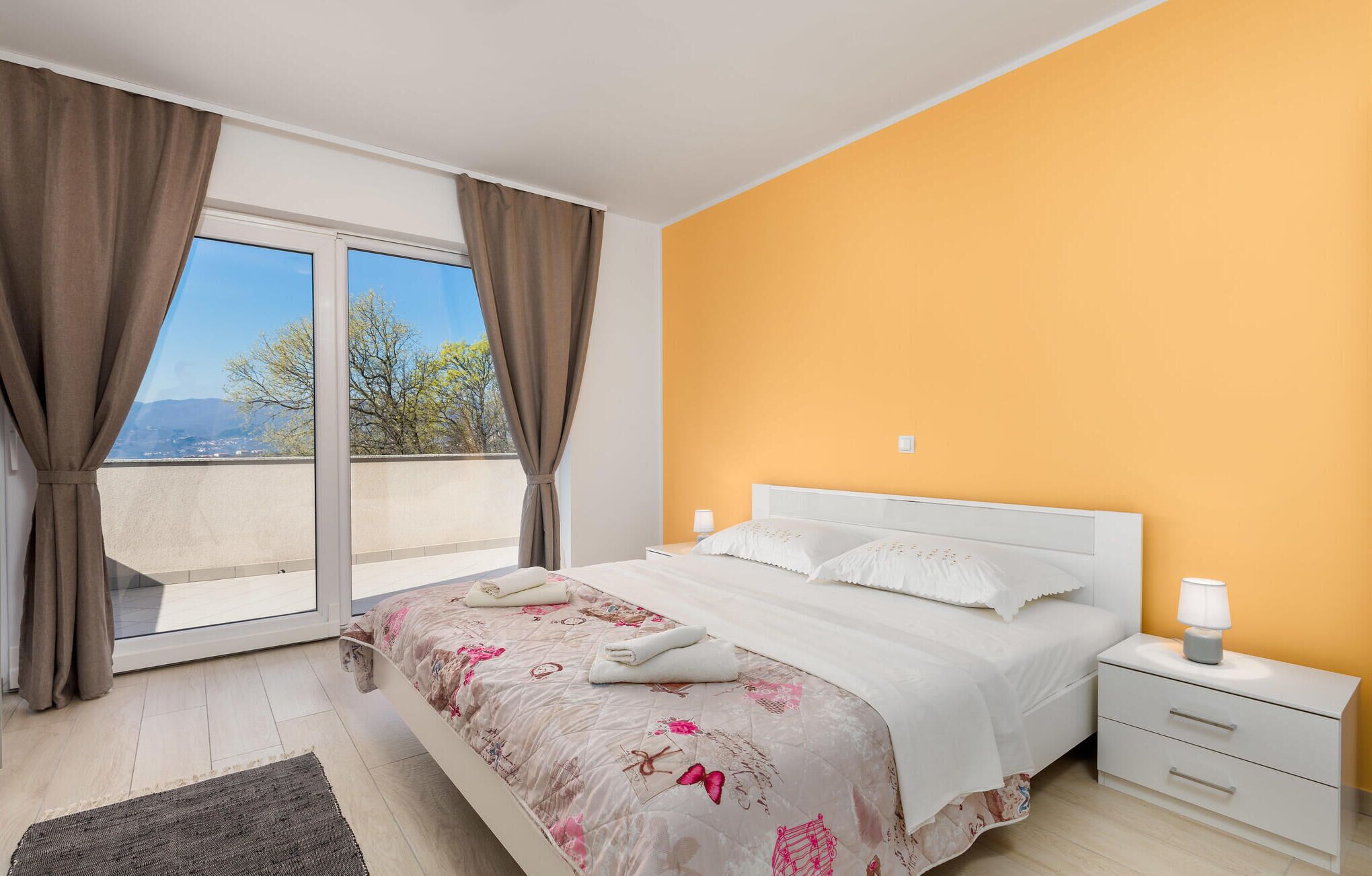 Ein Schlafzimmer mit Bett, Nachttisch und Blick durch ein großes Fenster.