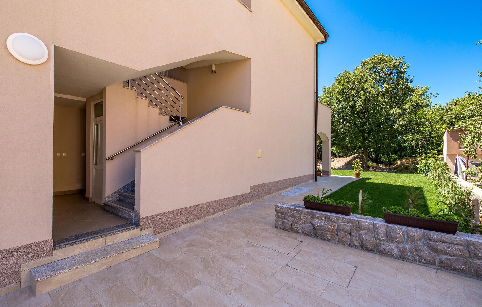 A modern building with a staircase leading to an entrance, a stone pathway, and a well-maintained garden area.