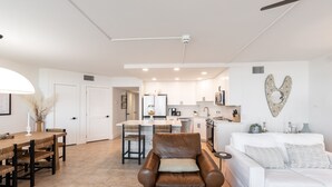 A modern kitchen with white cabinets, a central island, and a dining area with a wooden table and chairs. - Sandpiper Condominiums 208, Panoramic Gulf Views w/ direct access to Mustang Island/Port A beaches. (Port Aransas)