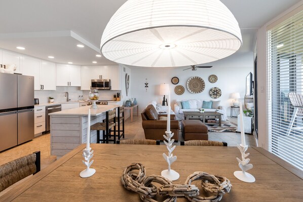 A modern kitchen with white cabinets, a wooden dining table, and a large pendant light.