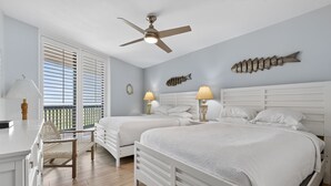 Een slaapkamer met twee bedden, een plafondventilator en een balkon met witte luiken.