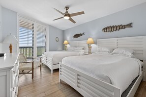 A bedroom with two beds, a ceiling fan, and a balcony with white blinds.