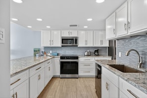 A modern kitchen with white cabinets, a stainless steel oven, a microwave, and a granite countertop.