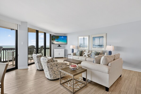 A modern living room with a balcony, a television, two framed pictures, and a sofa. - Sandpiper Condominiums 1105T, Panoramic Gulf View w/ direct access to Mustang Island/Port A beaches. (Port Aransas)