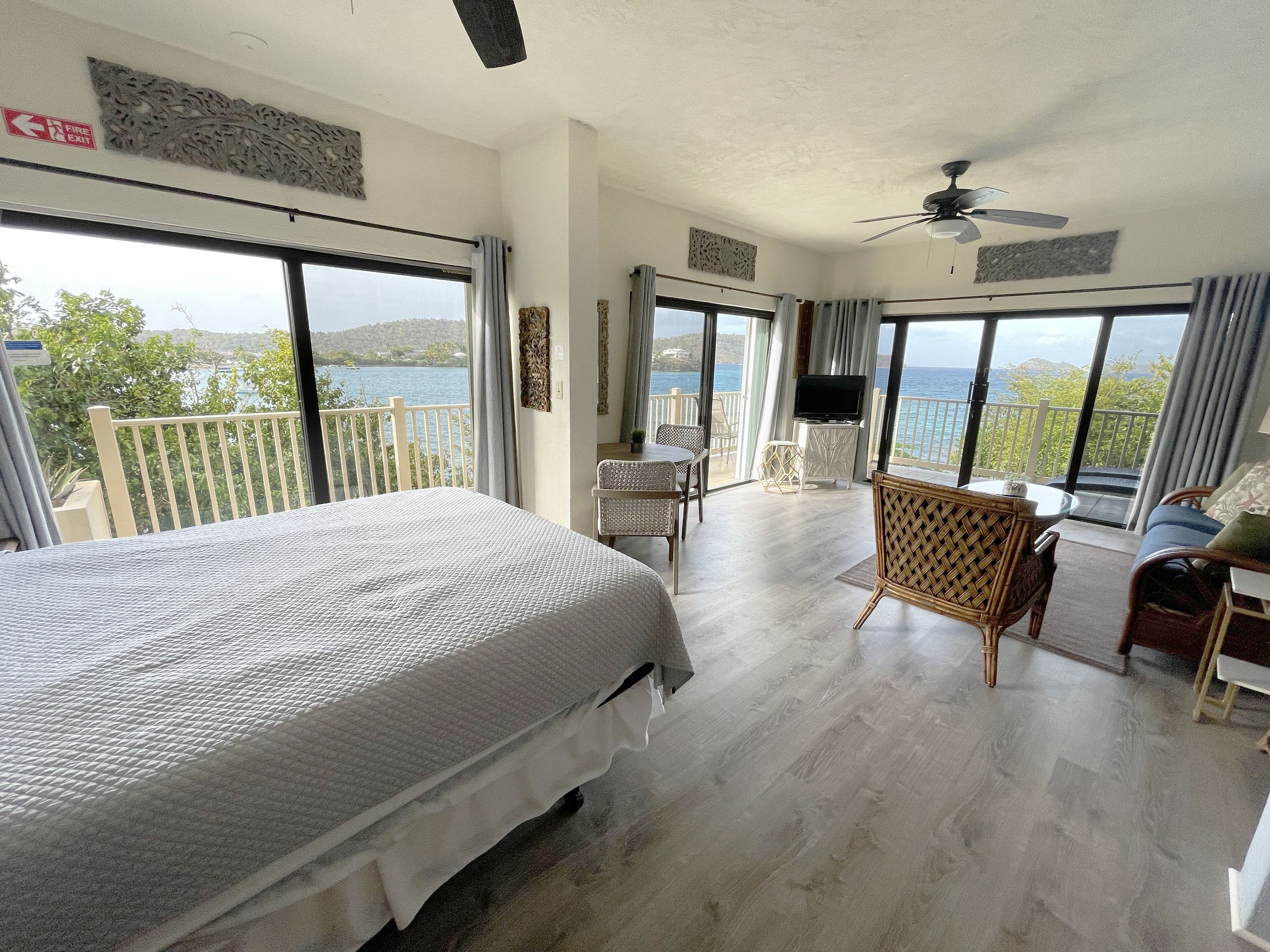 A bedroom with a large bed, a TV, and a balcony with a view of the sea.