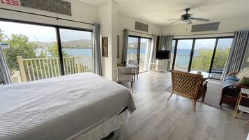 A bedroom with a large bed, a TV, and a balcony with a view of the sea.