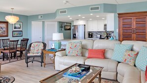 A living room with a sofa, coffee table, and dining area with chairs. - Sandpiper Condominiums 107L, Panoramic Gulf Views w/ direct access to Mustang Island/Port A beaches. (Port Aransas)