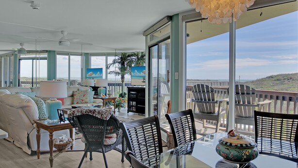 A spacious living area with a balcony overlooking the beach, furnished with a sofa, chairs, and a dining table. - Sandpiper Condominiums 107L, Panoramic Gulf Views w/ direct access to Mustang Island/Port A beaches. (Port Aransas)