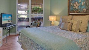A bedroom with a bed, a TV, a desk, and a window with blinds. - Sandpiper Condominiums 107L, Panoramic Gulf Views w/ direct access to Mustang Island/Port A beaches. (Port Aransas)