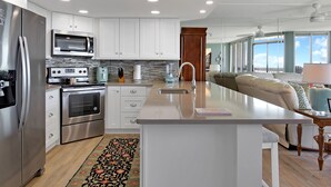 A modern kitchen with stainless steel appliances, white cabinetry, and a large island. - Sandpiper Condominiums 107L, Panoramic Gulf Views w/ direct access to Mustang Island/Port A beaches. (Port Aransas)
