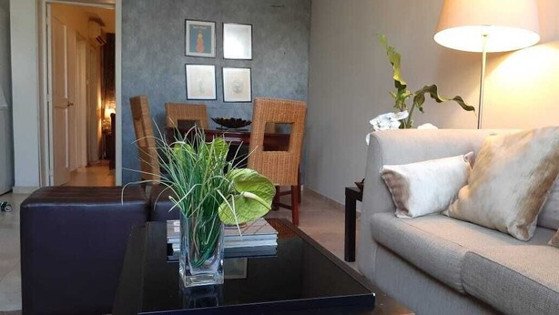 Un salon avec une table basse en verre, un canapé, une lampe et des tableaux encadrés accrochés au mur.