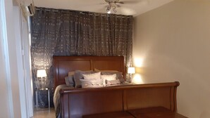 Une chambre avec un lit en bois, deux lampes de chevet, un banc en bois et un ventilateur de plafond.
