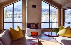 Una habitación acogedora con chimenea, ventanas amplias y vistas a un paisaje montañoso nevado.