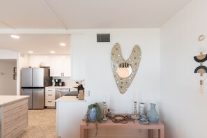 A modern kitchen with white cabinets, a stainless steel refrigerator, and a heart-shaped mirror.
