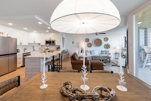 Una cocina moderna con armarios blancos, una mesa de comedor de madera y una lámpara colgante grande.