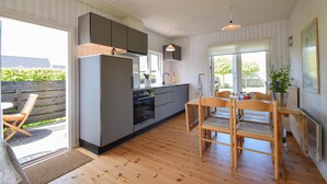 Eine moderne Küche mit grauen Schränken, einem eingebauten Backofen und einem Essbereich mit Holztischen und einer Tischplatte.