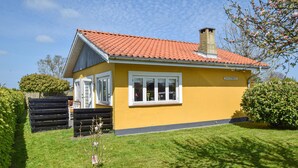 Ein gelbes Haus mit rotem Ziegeldach, einem Schornstein und einem kleinen Garten mit Holzzaun und Baum.