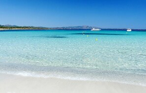A beach with clear turquoise water, a sandy shore, and boats in the distance. - Beach front apartment in Golfo Aranci (Golfo Aranci)