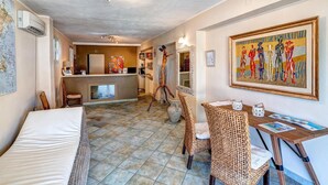 Une chambre d'hôtel avec un lit, un bureau, des fauteuils en osier, une carte accrochée au mur et un tableau.