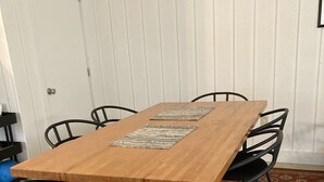 Een rechthoekige houten eettafel met zwarte stoelen, een decoratieve tafelkleed en een rood tapijt met patroon op een betegelde vloer.