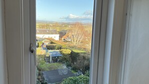 Ein Fenster mit Blick auf einen Garten und Häuser. Auf der Fensterbank stehen zwei Vasen mit Blumen.