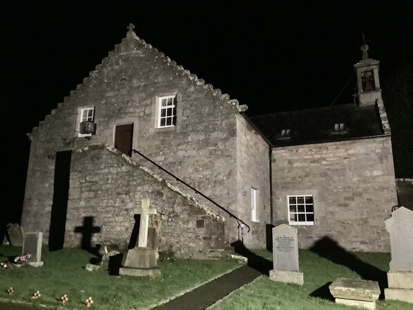 A stone building with a steeply pitched roof, a small staircase leading to a door, and a visible window.