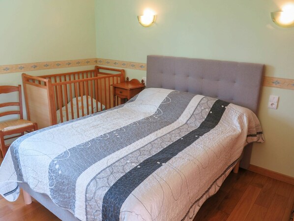 A bedroom with a bed, a wooden crib, a nightstand, and a chair.
