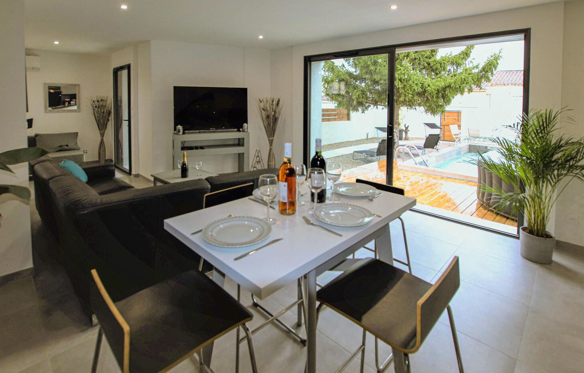 Un salon moderne comprenant un coin repas, un téléviseur à écran plat et une vue sur une piscine extérieure et un jardin.