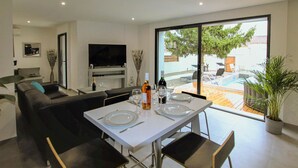 A modern living room with a dining area, a flat-screen TV, and a view of an outdoor pool and garden. - Beautiful home in Salon de Provence (Salon de Provence)