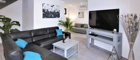 A modern living room with a black leather sofa, a coffee table, a flat-screen TV on a stand, and a large potted plant.