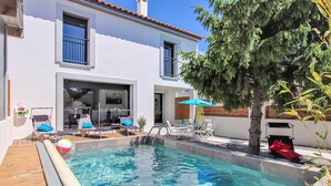 A pool area with lounge chairs and a table, surrounded by a white building with a tiled roof. - Beautiful home in Salon de Provence (Salon de Provence)