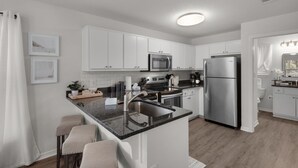 Una cocina moderna con armarios blancos, electrodomésticos de acero inoxidable, encimera negra y una pequeña isla con taburetes de bar.